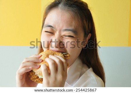 Asian woman age 28 years old in uniform eating chicken burger, junk food.