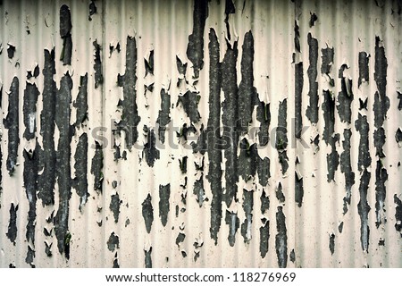 Grungy peeling painted metal background with discolored white paint flaking off a corrugated iron surface