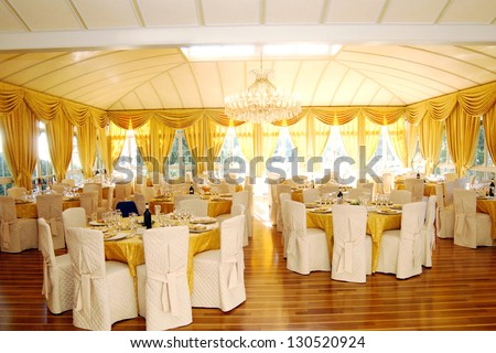 Luxury wedding or function venue interior with tables and table settings highlighted in a rich gold and multiple windows giving a bright airy light