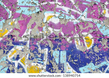 Colorful remnants of peeling graffiti with the paint peeling off the surface of the cement wall in a background texture and pattern