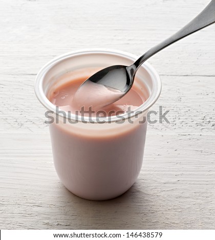 Plastic tub of healthy fruit yogurt with a spoon made by fermenting heated milk with a bacterial culture to produce a food rich in protein and calcium