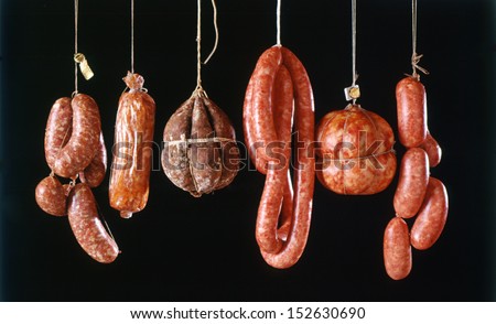 Assortment Of Different Types Of Fresh Spicy Italian Sausages Hanging Out To Cure And Dry In A Butchery Against A Black Background
