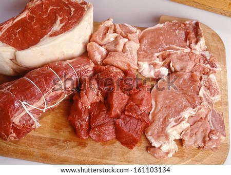 Assorted raw uncooked cuts of red meat displayed on a wooden board with beef and pork, high angle view