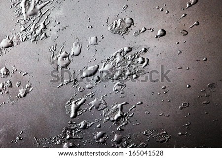 Grunge background of grey congealed splattered paint splodges on canvas in a random pattern side lit to enhance the texture