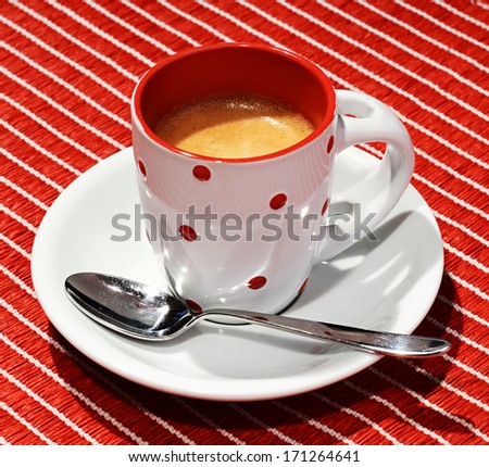 Pretty polka dot cup of rich freshly brewed aromatic Italian espresso coffee on a matching red striped background
