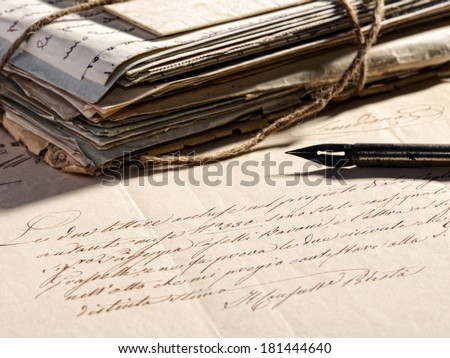 Writing a letter concept with a retro fountain pen lying on a faded old letter and a stack of vintage aged and worn correspondence tied with string