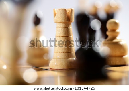 Game of chess with a selective focus view between chess pieces of a light wood castle in the center of the board