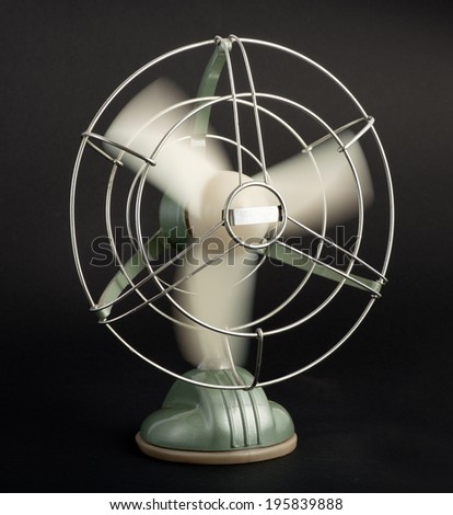 Vintage tabletop electric fan with a wire cage protecting the spinning blades creating a cooling airflow, on a black background