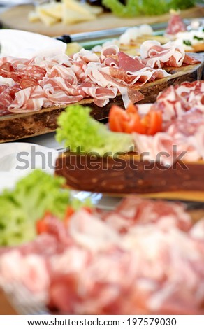 Variety of spicy Italian salami and cured ham on a buffet table with additional platters of assorted cold meat, focus to the salami and ham