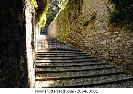 Long flight of deserted cobbled steps in Bellagio, Lake Como, Italy between old stone walls ascending the hillside towards lush greenery