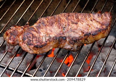 Grilled or barbecued beef steak sizzling on the grill over red hot coals on a fire