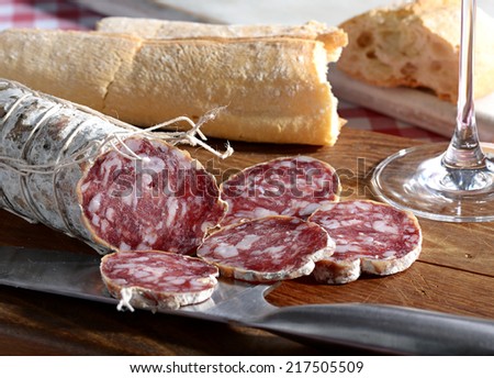 Sliced spicy seasoned Italian salami sausage and fresh bread or baguette on a wooden table for a rustic lunch or snack