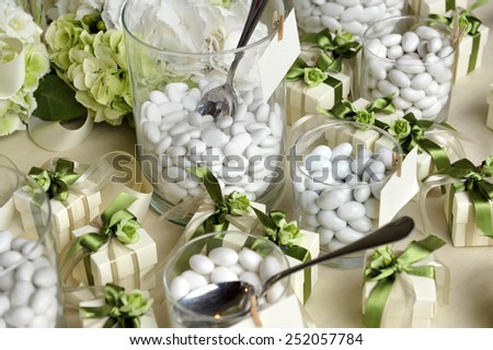Close up White Sugared Almonds on Small Glasses and Small Gift Boxes with Green Ribbons on Top of the Table.