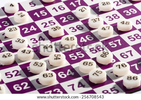 Close up White Plastic Bingo Numbers on Top of a White and Purple Bingo Game Card