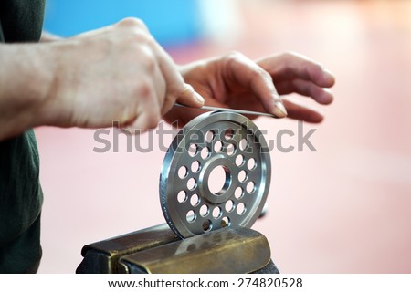 Male hands smoothing with a file the edge of a metallic wheel with round holes, fixed in a vise bench tool