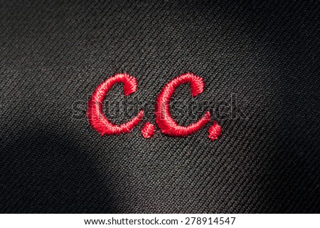 Embroidery of initials or clothing logo with C.C. in red stitching on a dark fabric in a needlework, tailor, seamstress or clothing manufacture concept