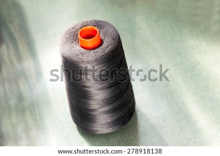 Dark cotton thread on an orange plastic upright bobbin or spool for sewing or embroidery machine, close-up with copy space on blurred green