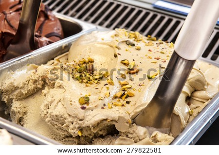 Delicious nutty pistachio ice cream sprinkled with roasted nuts on display in an ice cream parlour with a scoop for sale as takeaway summer desserts