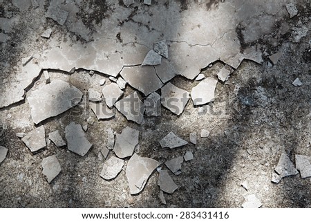 Cracked and broken cement paving lying scattered randomly on the ground in dappled shadow