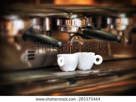 Italian espresso machine on a counter in a restaurant dispensing freshly brewed coffee into two small cups to be served to customers