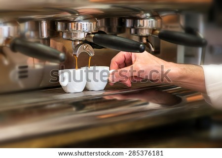 Close up view of the hand of a man working in a coffee house preparing espresso coffee waiting for the coffee machine to finish pouring the fresh beverage into two small cups