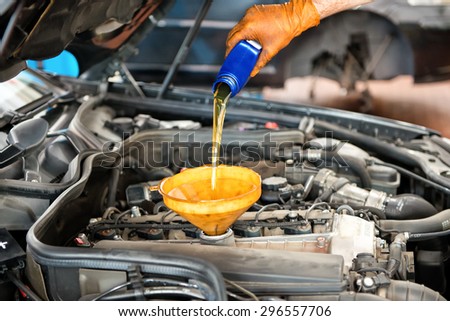 Mechanic topping up the oil in a car pouring a pint of oil through a funnel into the engine, close up of his hand and the oil