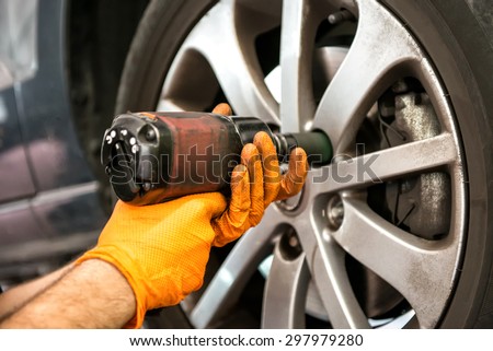 Mechanic working on a car wheel tightening or loosening the bolts on the hub and rim with an electric power tool, close up view of his hands