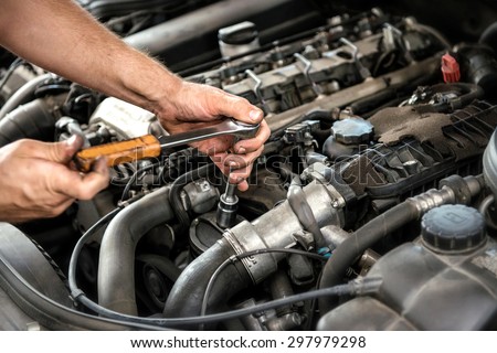 Mechanic using a wrench and socket on the engine of a motor car during a service or repair in an automotive workshop, close up of his hands