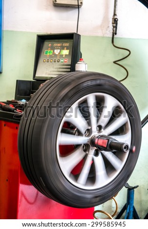 Balancing a rotating car tire on a machine in an automotive repair workshop or garage with a digital display showing the weights needed