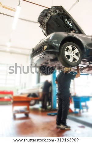 Motor mechanic working on a car on a hoist or lift in a repair workshop or garage during emergency repairs or a routine service