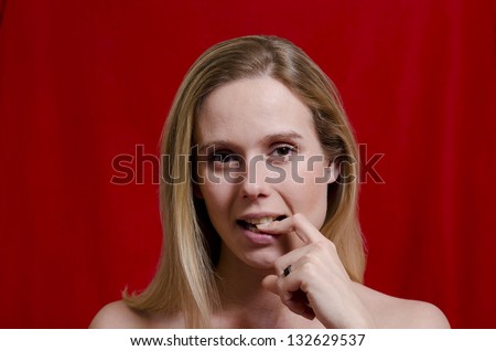 young blonde woman biting on a finger on red background