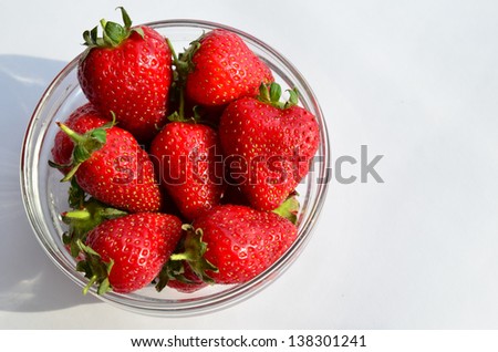 Strawberries in glass bowl in sunlight, with shadow, over white background