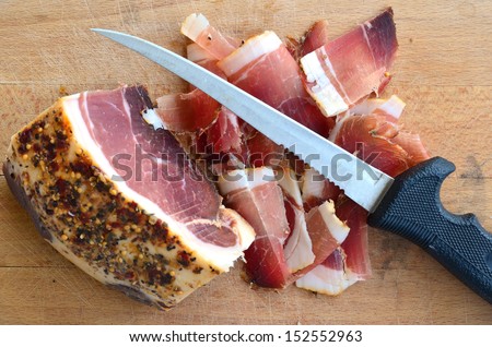 Homemade spicy prosciutto, smoked and dried in the wind for a long time on wooden chopping board, big piece and thin slices against white background