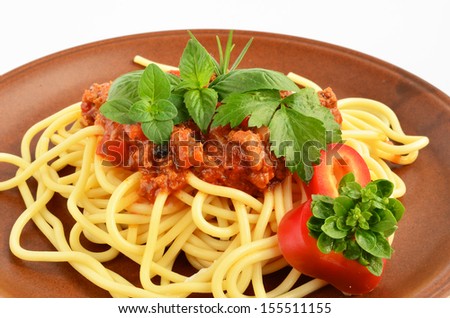 Spaghetti Bolognese with fresh herb spices - oregano, basil, rosemary, celery and red pepper, served on rustic, brown ceramic plate over white background