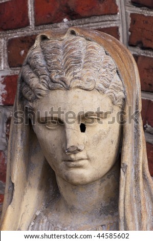 Holy Mary statue portrait. Ancient statue near a brick wall.