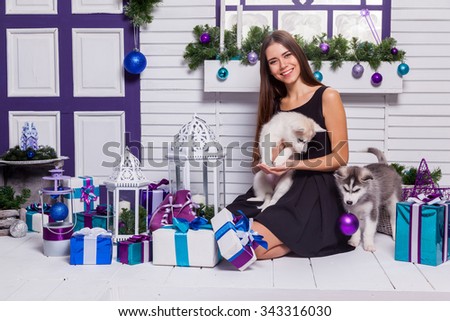 beautiful brunette in a black dress playing on the terrace with puppies Husky, close to the Christmas tree and gifts.