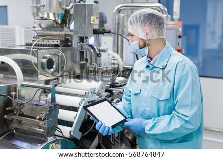 factory worker in lab suit with empty tablet stand near manufacture machine