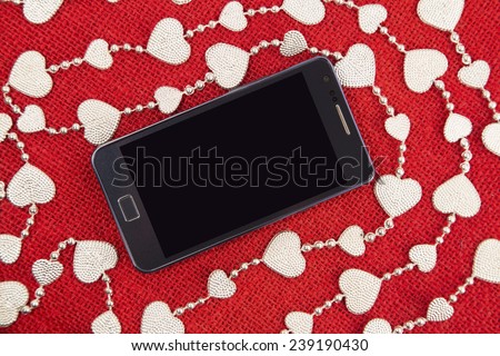 Mobile phone and the silver garland on a red burlap background