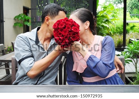 A couple, man and woman. kissing behind red roses bouquet