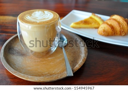 A cup of Hot Coffee, Croissant and Passion fruit Tart on wood table in a cafe