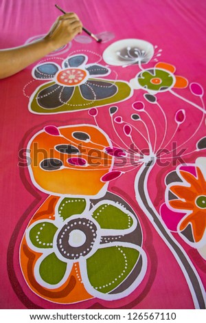 An artist carefully paint the floral/flower motif on a red silk batik fabric