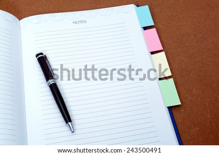 Blank notebook page with black ball pen and multi colored post it on wooden background