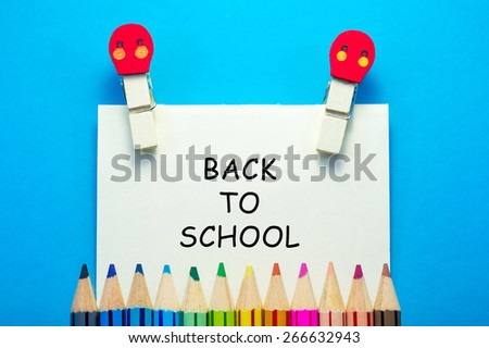 BACK TO SCHOOL words written on sticky note with clips and color pencils on blue background