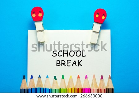 SCHOOL BREAK words written on sticky note with clips and color pencils on blue background