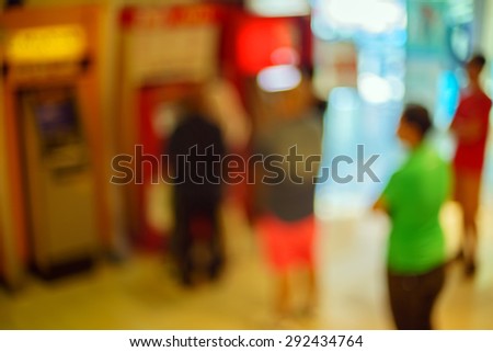 Blur image of people queueing at ATM machines in a mall with bokeh background