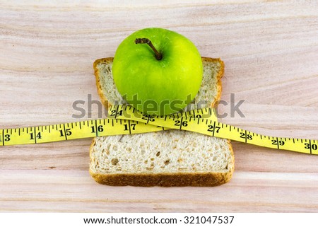 Apple on top of bread wrapped with measuring tape on wooden surface. Healthy diet concept. Selective focus.