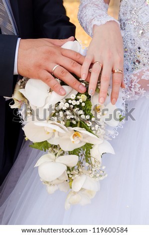 A newly wed couple place their hands on a wedding bouquet