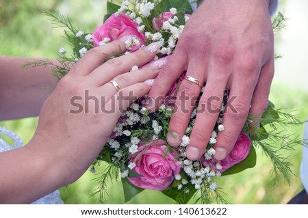 A newly wed couple place their hands on a wedding bouquet