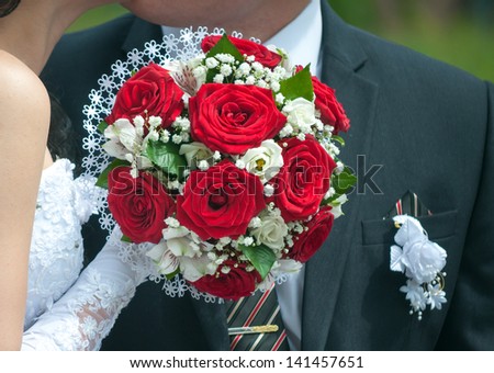 Wedding bouquet with red roses in hand of the bride against the background of the groom