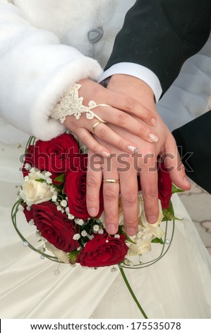 A newly wed couple place their hands on a wedding bouquet showing off their wedding bands.